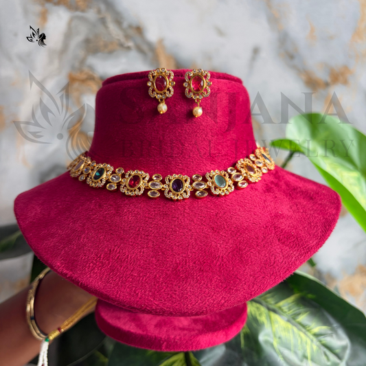 A bright magenta velvet hat displayed on a matching stand, decorated with a gold-toned ornate band featuring multicolored stones. A pair of matching gold-toned earrings with pearl drops is placed on top of the hat.