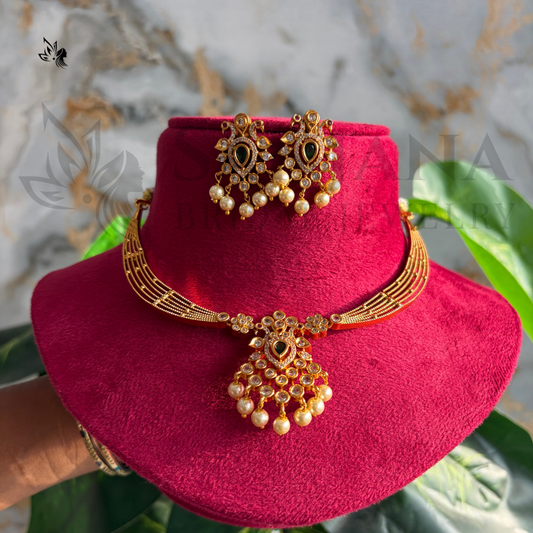 Gold-toned traditional Indian jewelry set including a necklace with a large pendant, matching earrings, and a bracelet, displayed on a magenta velvet stand with a marble background and green leaves.