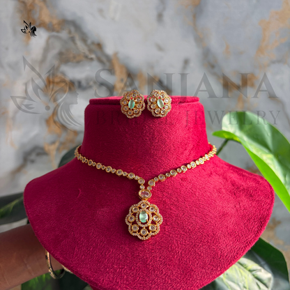 Gold-toned traditional necklace and matching earrings displayed on a bright pink velvet jewelry bust, with a marble-patterned backdrop and green leaves in the background.