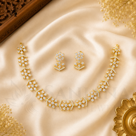 Gold-toned jewelry set with a floral necklace, matching earrings, and a headpiece arranged on draped cream satin fabric with decorative dried flowers and a brass vessel.
