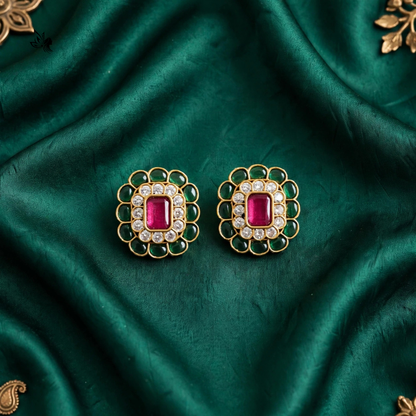A pair of gold-toned statement earrings with rectangular pink gemstones and clear stones, displayed on a draped emerald green satin fabric.