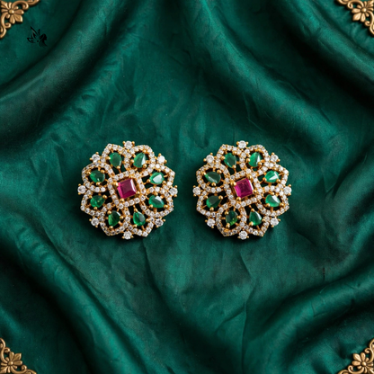 A pair of ornate gold-toned jewelry pieces with green and pink gemstones, displayed on a draped emerald green fabric background.