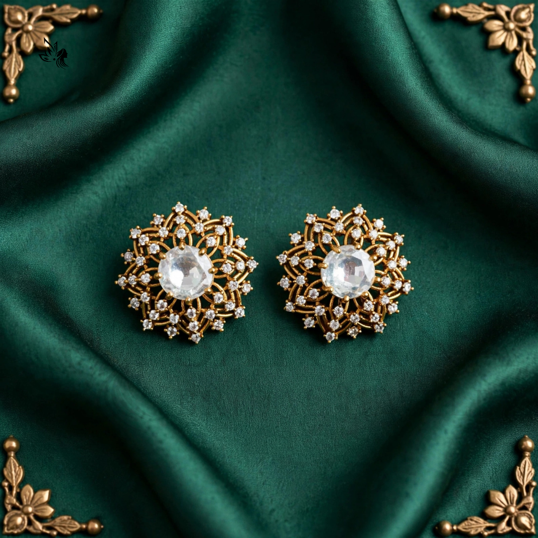 A pair of ornate gold-toned floral brooch pins with clear faceted center stones, displayed on a draped dark green satin fabric with decorative gold corner accents.
