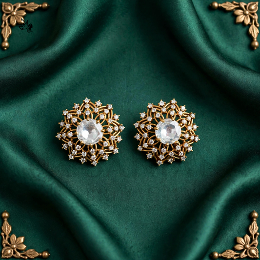 A pair of ornate gold-toned floral brooch pins with clear faceted center stones, displayed on a draped dark green satin fabric with decorative gold corner accents.