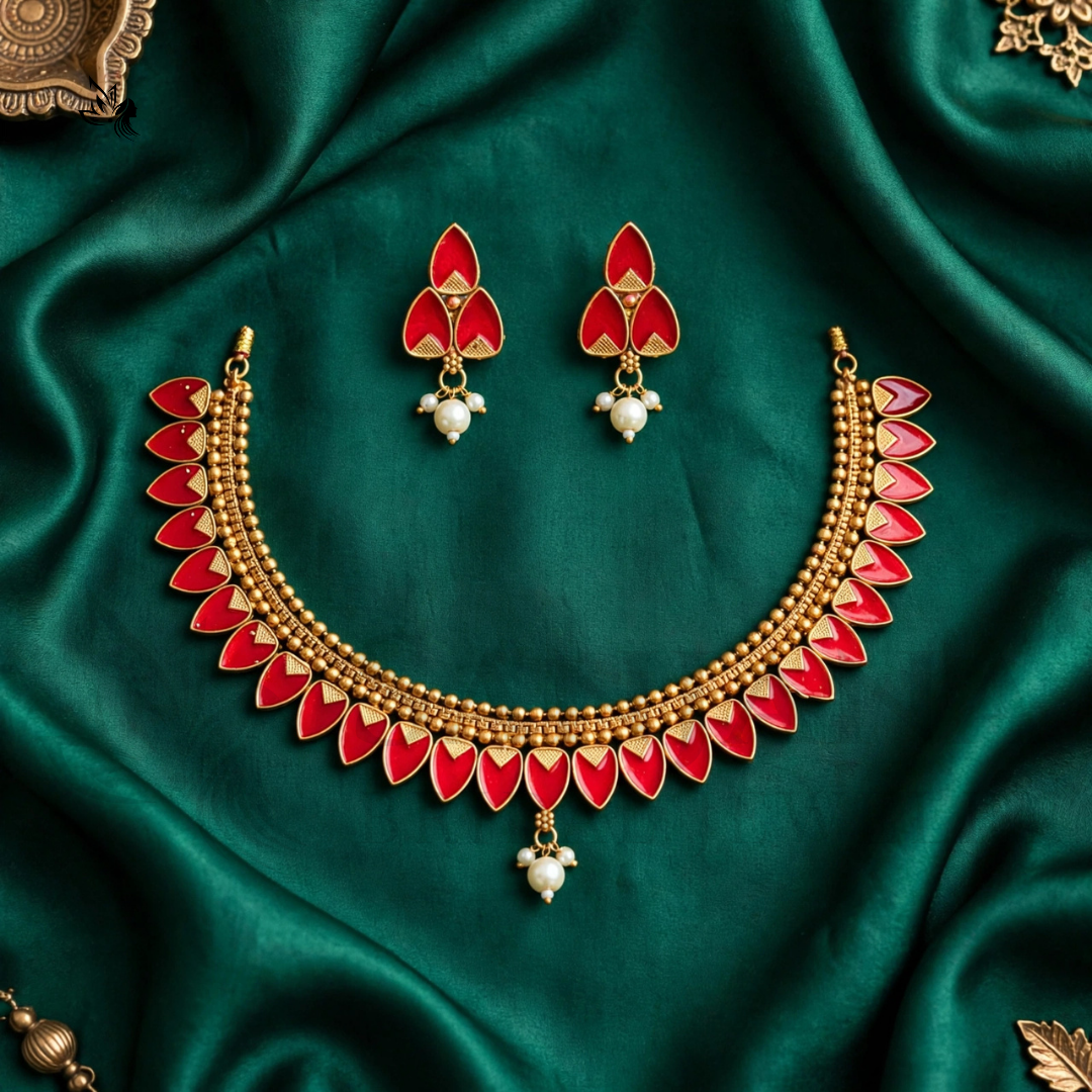 Gold-toned traditional necklace and matching earrings with red enamel petal details and white pearl-like drops, arranged on draped emerald green satin fabric.