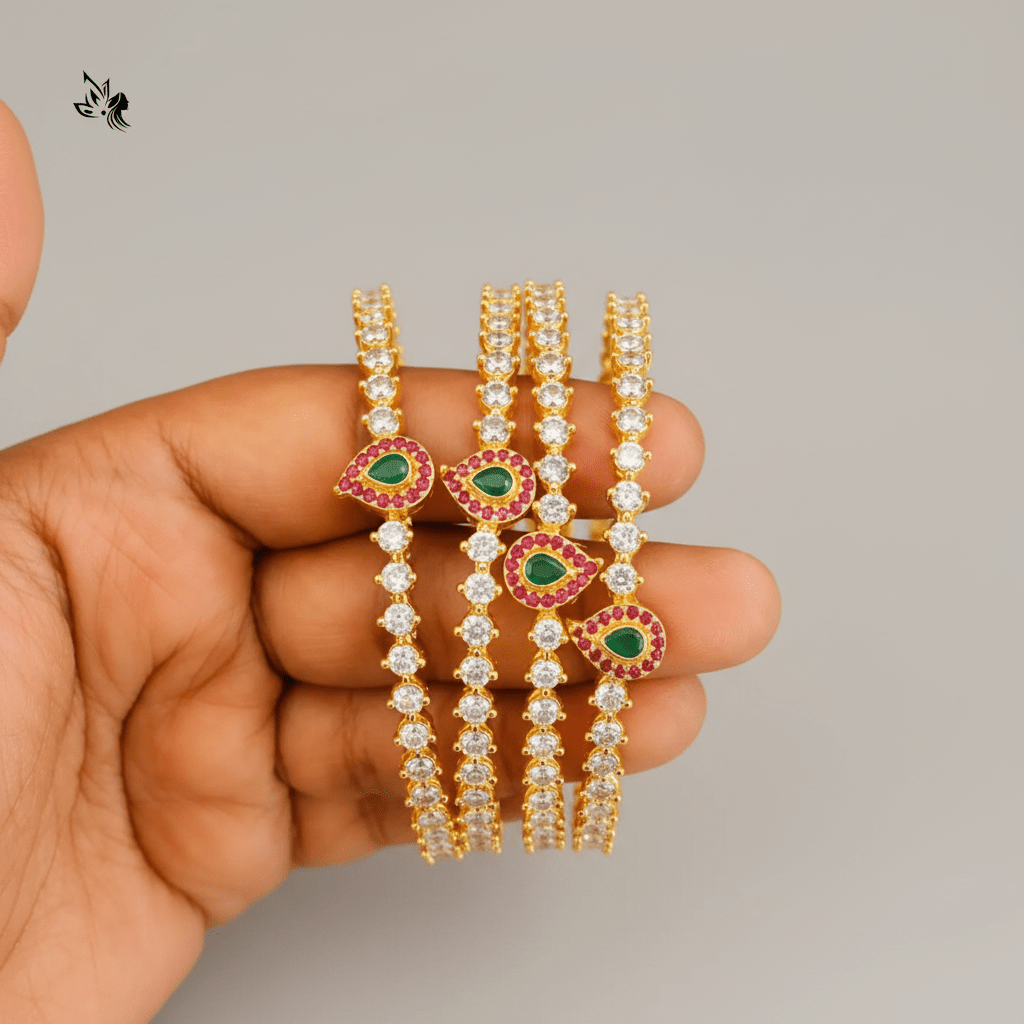 Gold and diamond bangles with green gemstones held in a hand on a beige fabric background.