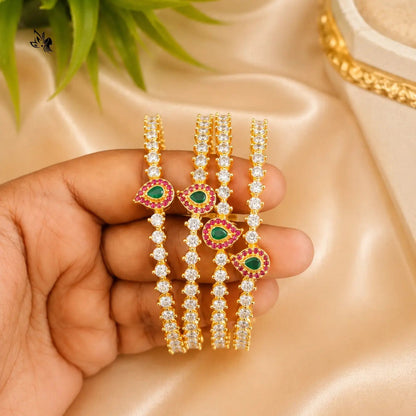 Gold and diamond bangles with green gemstones held in a hand on a beige fabric background.