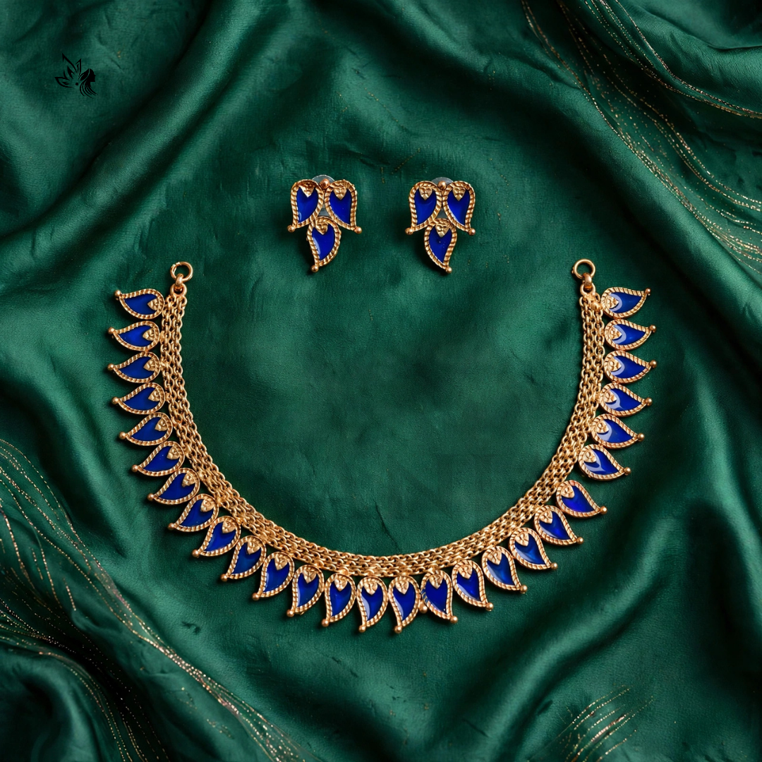 Gold-toned necklace and matching stud earrings with deep blue enamel leaf motifs, arranged on a draped emerald green satin fabric background.