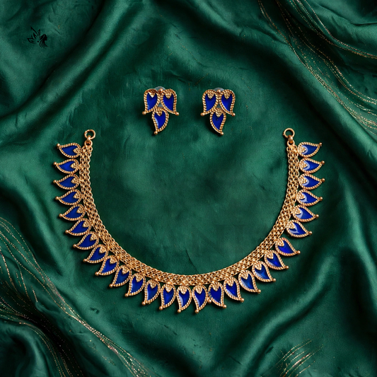 Gold-toned necklace and matching stud earrings with deep blue enamel leaf motifs, arranged on a draped emerald green satin fabric background.