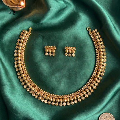 Gold-toned traditional necklace and matching rectangular earrings displayed on draped emerald green satin fabric, with a coin in the corner for scale.