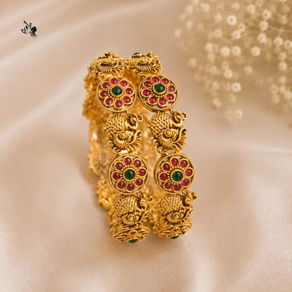 Gold earrings with red and green gemstones on a beige background