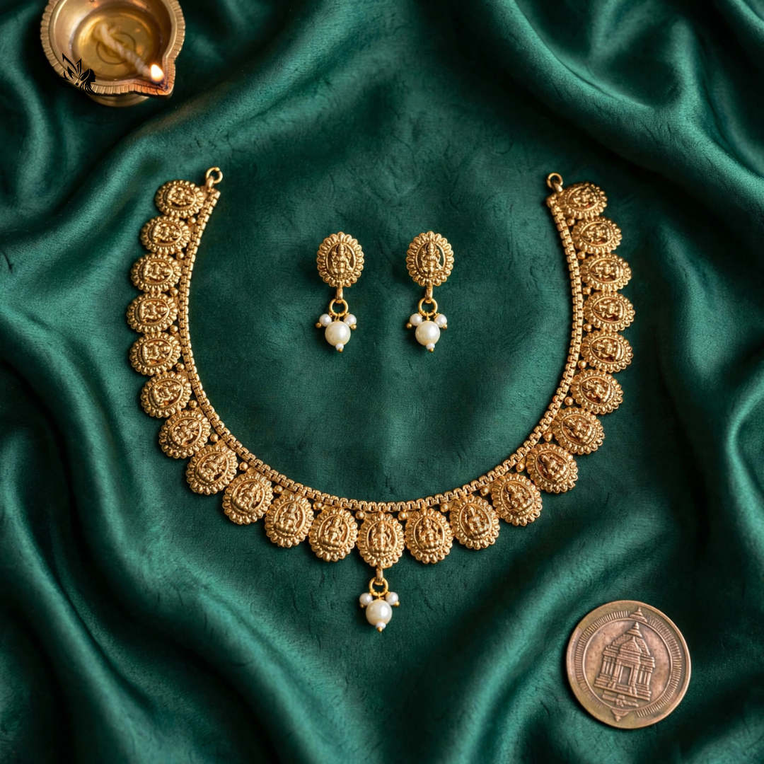 An ornate gold-toned jewelry set arranged on draped emerald green satin fabric, including a necklace, matching earrings, and a coin placed nearby for scale.