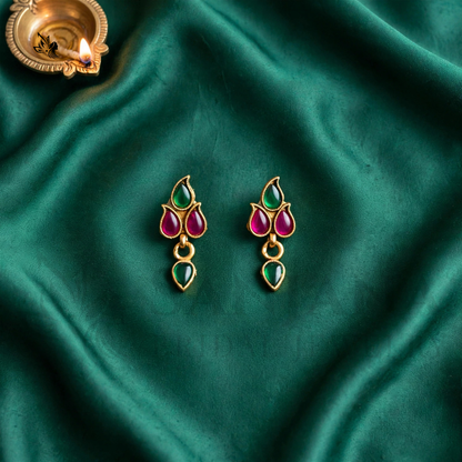 Traditional gold-toned Kemp drop earrings with green and magenta stones on emerald green fabric.