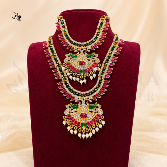 A traditional Indian gold-plated necklace with red, green, and white stones, displayed on a dark red velvet jewelry stand against a cream satin background.