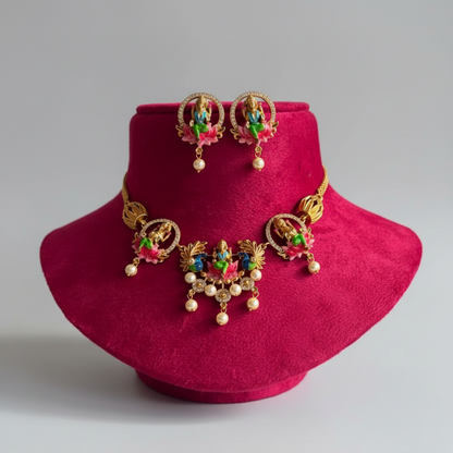 Gold-toned traditional jewelry set displayed on a magenta velvet jewelry bust, including a necklace, matching earrings, and a central pendant, with pink, green, and blue enamel details and pearl-like beads.